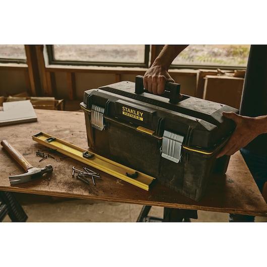 STANLEY 023001W toolbox on workbench with hammer, nails, and level, person holding handle, workshop background.