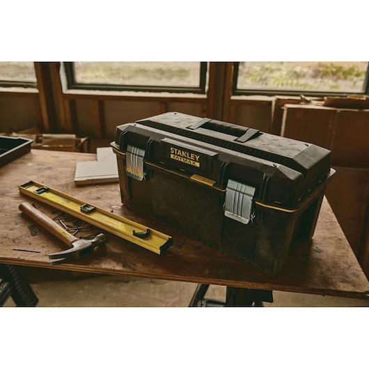 Stanley 023001W toolbox with metal latches on a workbench, hammer and level nearby, workshop setting.