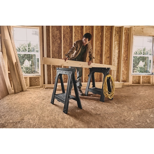 STANLEY 060864R plastic sawhorses in use at construction site, supporting wooden beam and yellow cord.