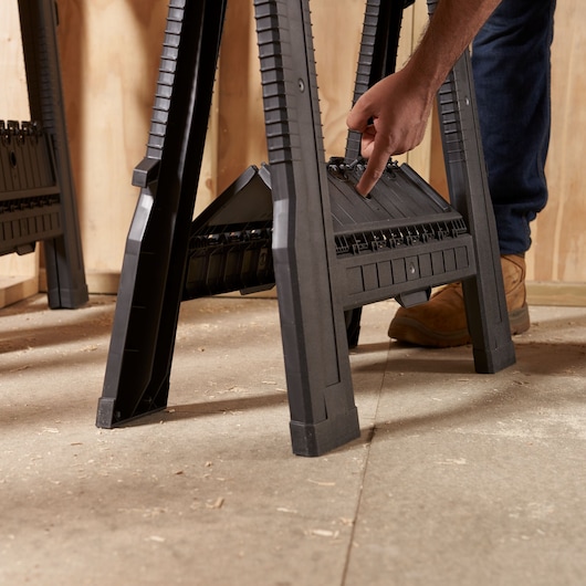STANLEY 060864R black plastic sawhorse in workshop, close-up side angle with hand adjusting center shelf.