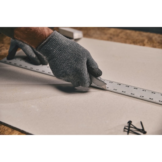 STANLEY 10-299 utility knife cutting along a metal ruler on a sheet, close-up hand with glove.