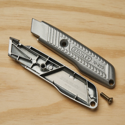 STANLEY 10-299 utility knife metal housing shown disassembled with screw, on wood surface.