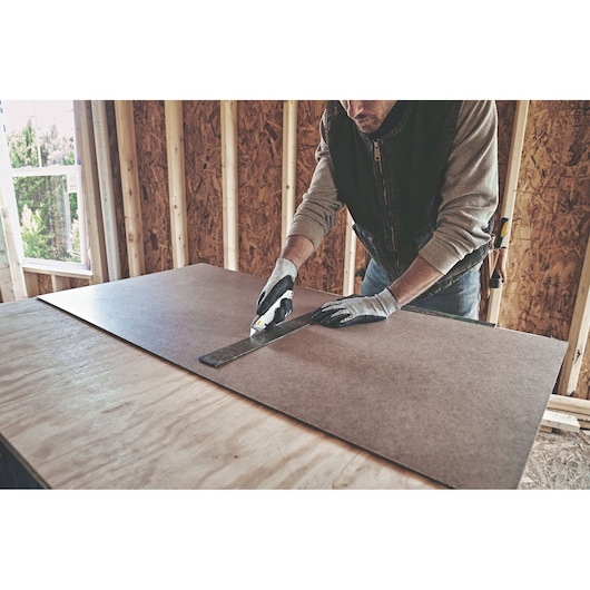 STANLEY 10-499 utility knife cutting board material along metal ruler, construction site setting.