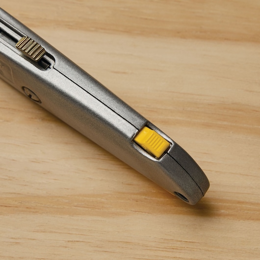 STANLEY 10-499 utility knife close-up showing yellow blade lock and metallic finish on wood surface.