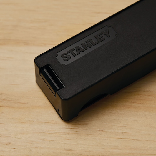 STANLEY 11-301L black plastic utility blade case, angled close-up on wood surface.