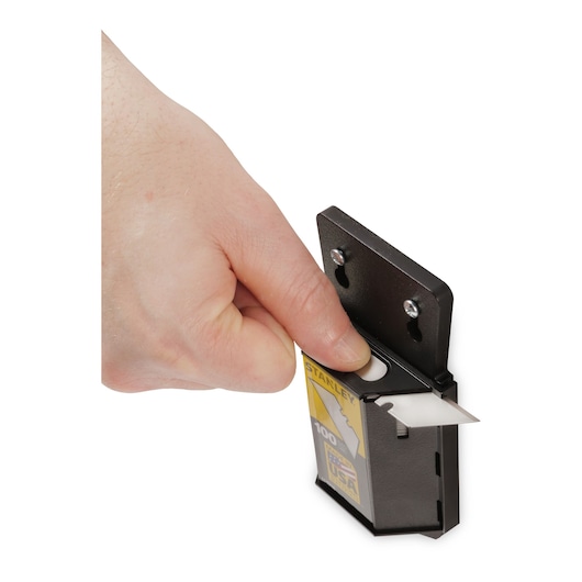 STANLEY 11-921A utility blade dispenser being used, hand removing a single utility blade from black wall-mounted holder.
