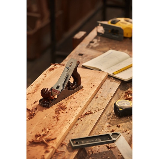 STANLEY 12-904 wood hand planer on wooden board, workbench with tape measure and notebook.