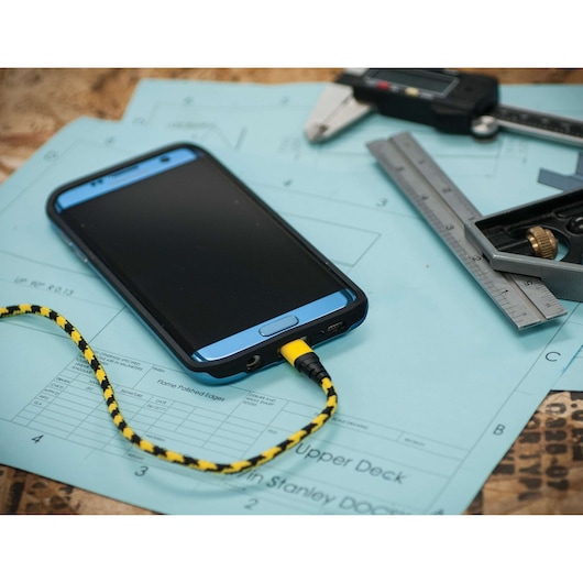 STANLEY 1319592ST2 photography of a braided yellow and black charging cable connected to a smartphone on blueprints.