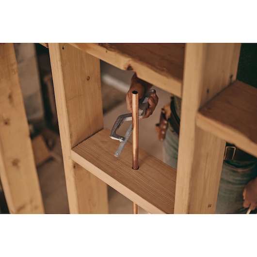 STANLEY 15-809 clamp holding copper pipe in wood framing, close-up product photography.