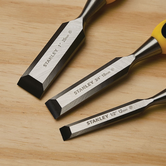 Photo of STANLEY wood chisels, SKU 16-300, three sizes with sharpened steel blades and yellow handles on wood surface.
