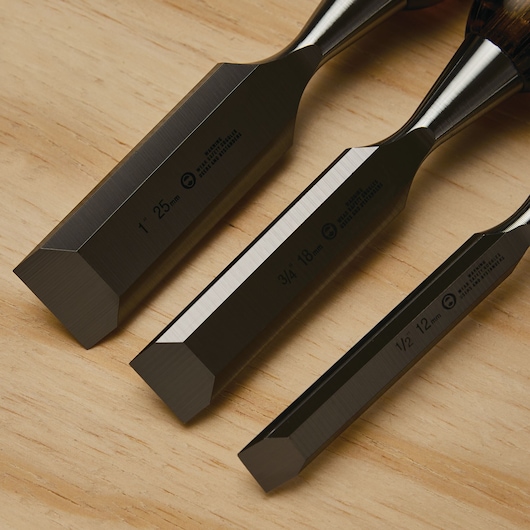 STANLEY 16-970 wood chisel set, close-up angle, showing three steel blades on light wood surface