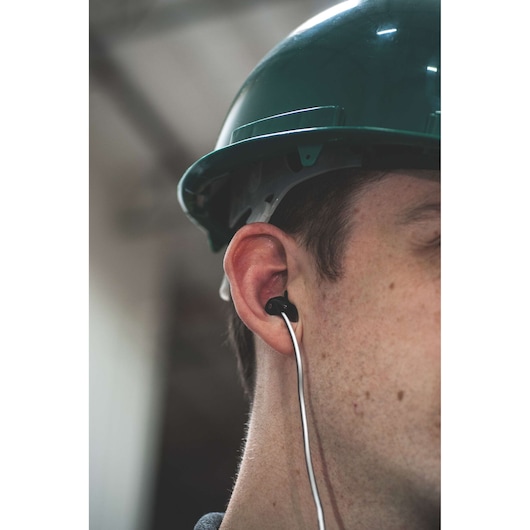 STANLEY 1909514ST2 photography of ear with black wired earbud and green hard hat, close-up angle.