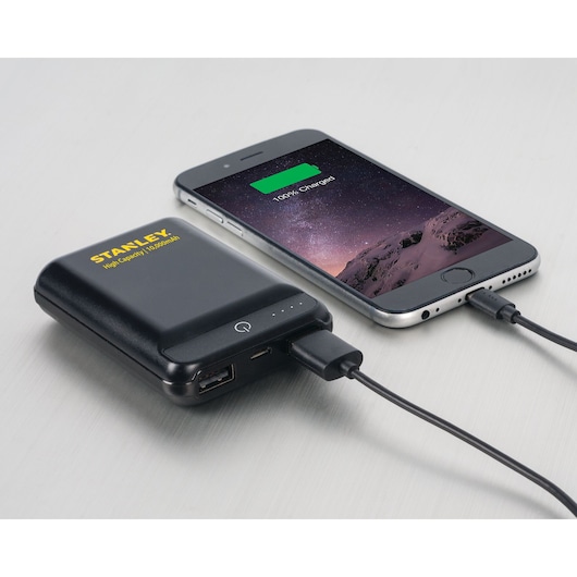 Stanley 2159011ST2 portable power bank charging a smartphone, angled view on light gray surface.