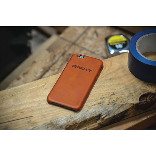 STANLEY 2159562ST2 brown phone case on wood workbench, with tape and measuring tool in background.