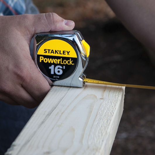 STANLEY 33-116 PowerLock tape measure in use measuring a wooden plank, close-up view.