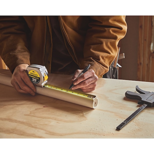 Stanley 33-425 PowerLock tape measure marking PVC pipe on workbench, photography close-up.