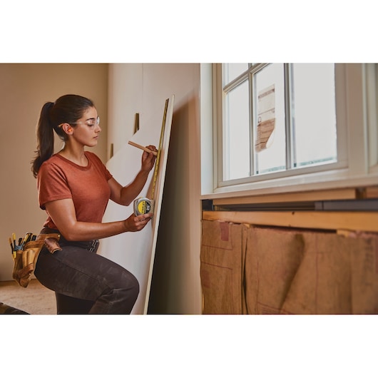 Stanley 33-425 tape measure held by worker marking drywall near window during construction.