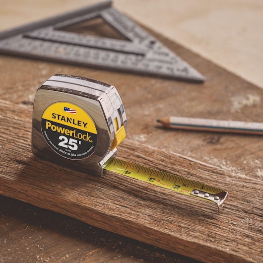 STANLEY 33-425 tape measure with yellow blade extended, shown on wood plank with pencil and square in background.