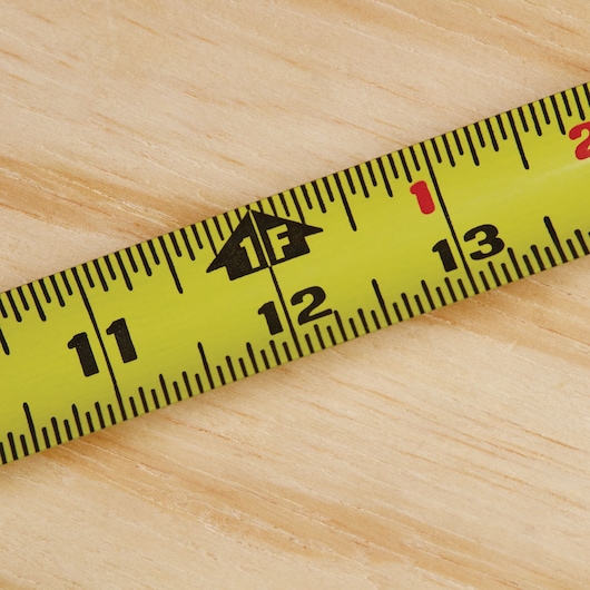 STANLEY 33-425 yellow tape measure with black and red markings on wood surface, close-up photography.