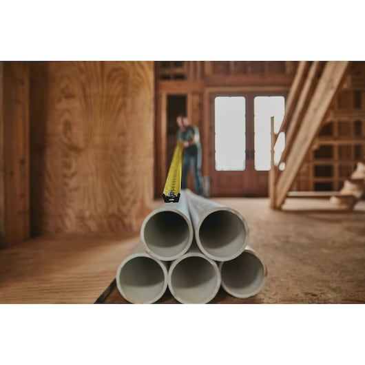 Stanley 33-725 tape measure extended across stacked pipes in a construction setting, side angle.