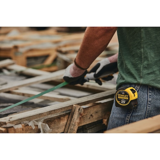 Photo of STANLEY 33-725 tape measure clipped to jeans, person working with wood.