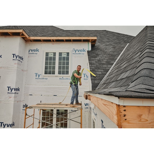 STANLEY 33-725 tape measure in use by a worker measuring roof edge on a construction site, angled side view.