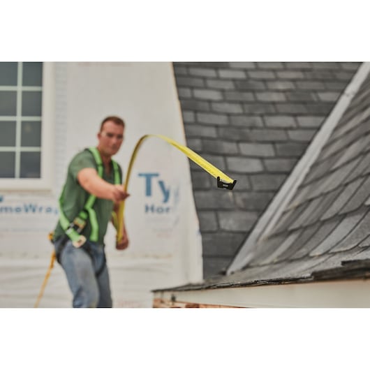 STANLEY 33-725 tape measure extended by a worker in a harness next to a sloped roof, construction setting.