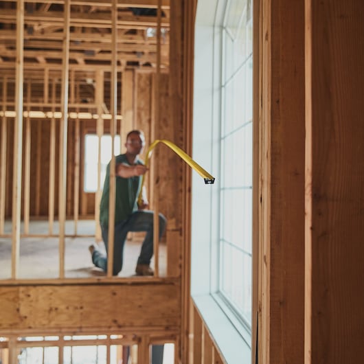 STANLEY 33-725 tape measure extended across wood framing in construction site, person kneeling and measuring.