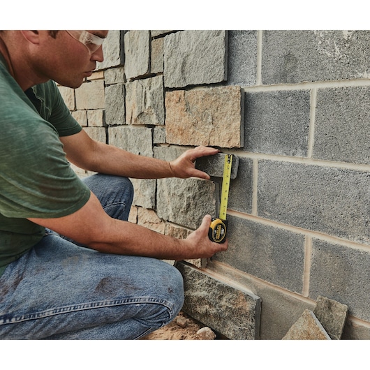 STANLEY 33-725 tape measure used by person measuring stone wall, close-up outdoor photography.