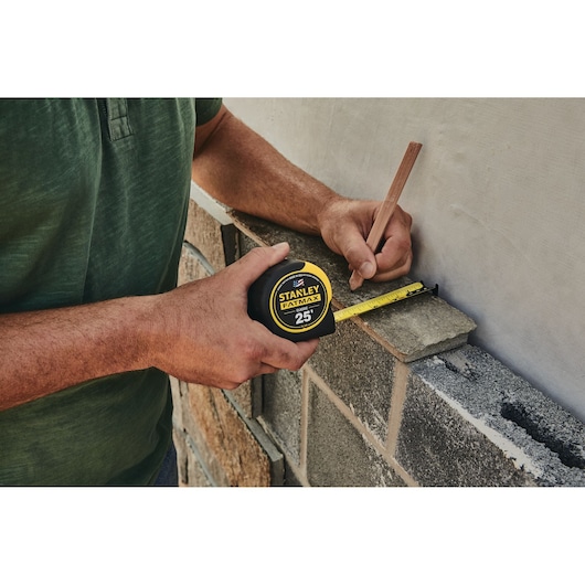 Photo of STANLEY 33-725 tape measure in use, measuring a concrete block wall with a pencil marking the measurement.