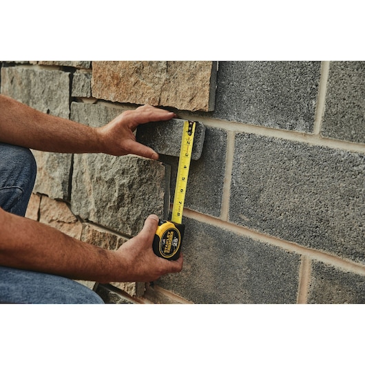 Photo of a person measuring a stone wall with a STANLEY 33-725 tape measure.