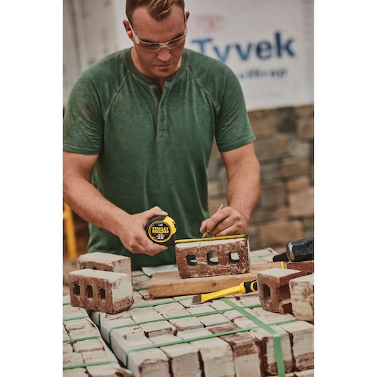 STANLEY 33-725 tape measure in use on a construction site, measuring a red brick on a stack of bricks.