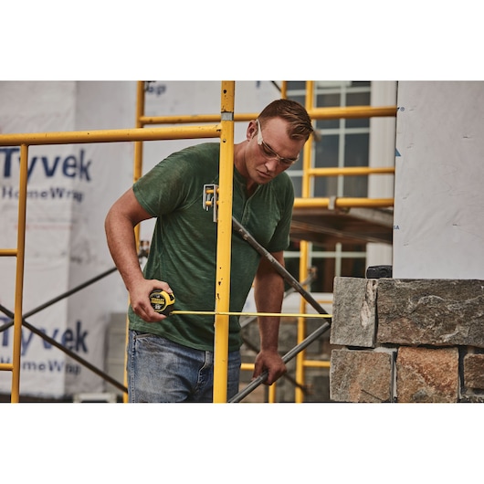 STANLEY 33-725 tape measure in use at construction site with scaffolding and stone wall.