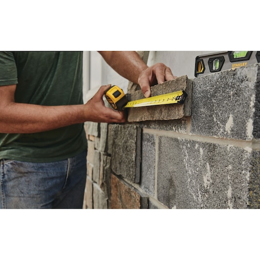 STANLEY 33-725 tape measure used to measure stone on wall, carpenter's hands visible, close-up photo.