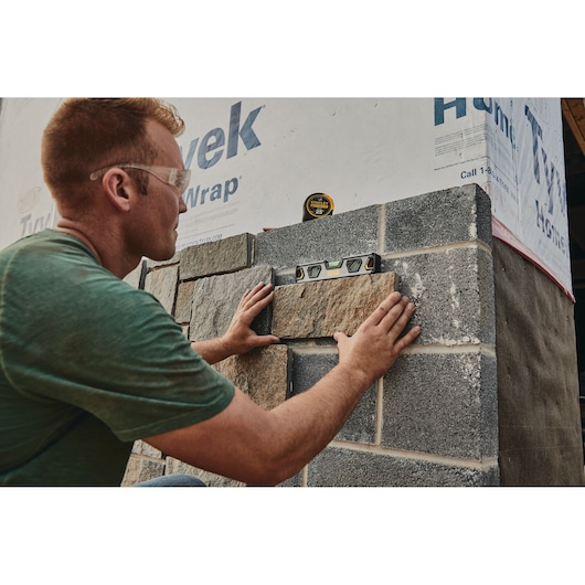 STANLEY 33-725 tape measure on stone wall with level tool, person aligning stones, construction site.