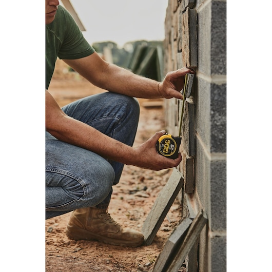 STANLEY 33-725 tape measure held by a person measuring concrete blocks at a construction site, outdoor angle.