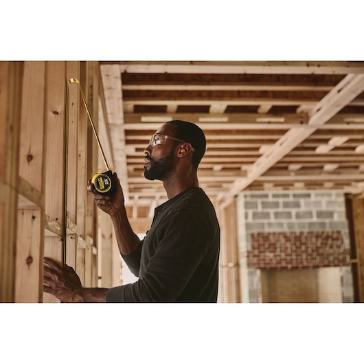STANLEY 33-725 tape measure used to measure wooden studs in a construction framing setting.