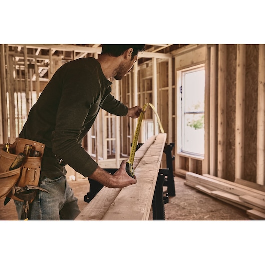 STANLEY 33-725 tape measure used to measure wooden plank in construction site, side angle photography.