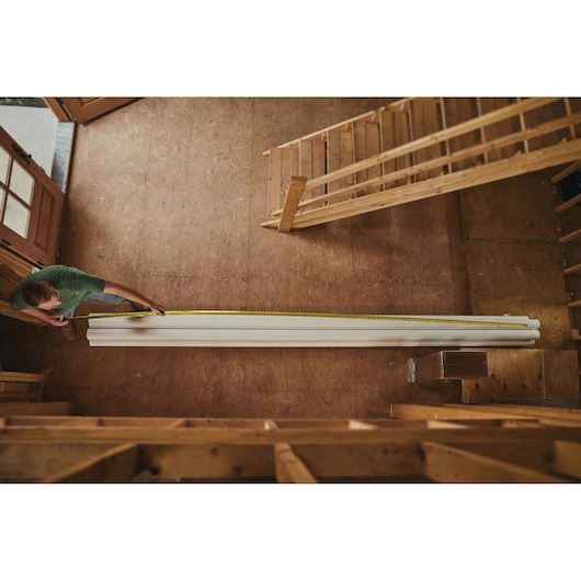 STANLEY 33-725 tape measure extended to measure long white boards in a wood workshop, top-down view.