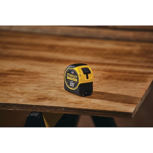 STANLEY 33-725 tape measure, yellow and black, 25 ft, on wooden surface, angled view.