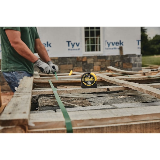 STANLEY 33-725 tape measure on a construction site with worker in background, outdoor setting.