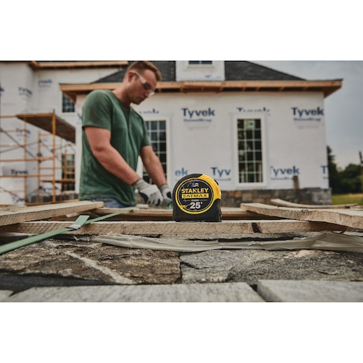 STANLEY 33-725 tape measure on stone surface at construction site, home under renovation in background.