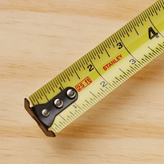 Stanley 33-725 tape measure with yellow blade and metal tip, close-up on wooden surface.