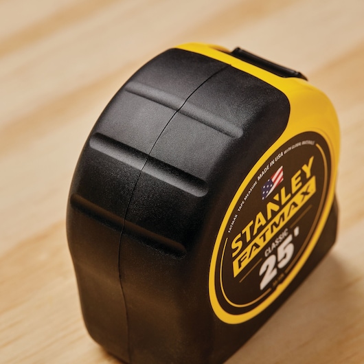 Photo of STANLEY 33-725 tape measure, black and yellow case, side angle, on wooden surface.