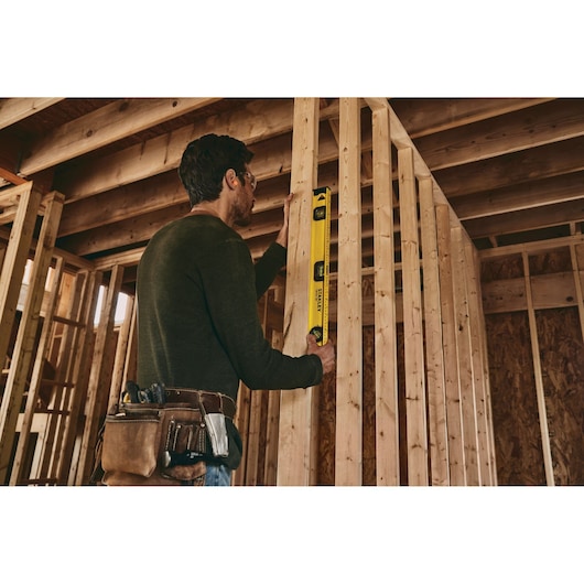 STANLEY 42-324 level tool used by worker checking vertical alignment of wooden studs at construction site.