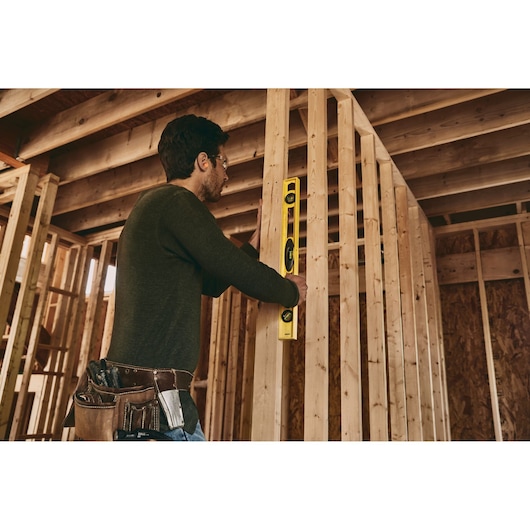STANLEY 42-468 level tool used by worker in unfinished wood frame structure, side angle photo.