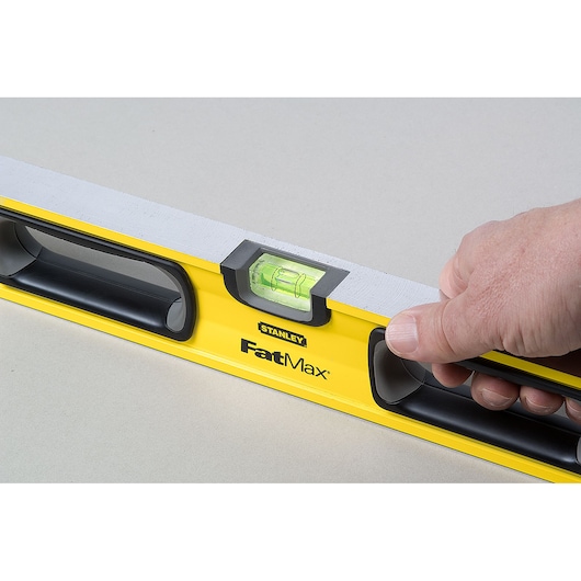 STANLEY 43-524 level tool, yellow FatMax model, side view, hand holding black handle.