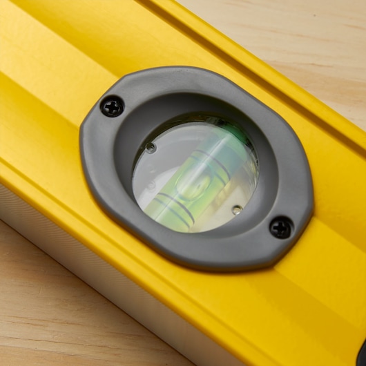 STANLEY 43-524 yellow level tool close-up showing bubble vial and gray frame, angled on wood surface.