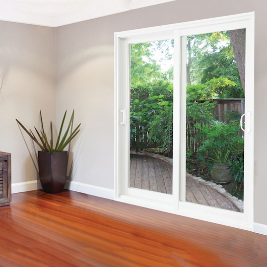 STANLEY 500001 sliding glass door with white frame, interior view, showing wood floor and outdoor greenery.
