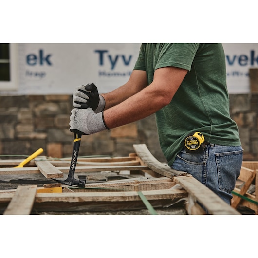 Photo of person using STANLEY 51-167 claw hammer on wooden boards at construction site, wearing gloves and jeans.